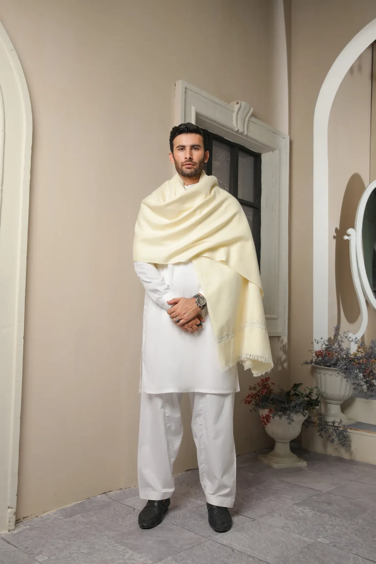 Man in a cream wool shawl standing in a courtyard